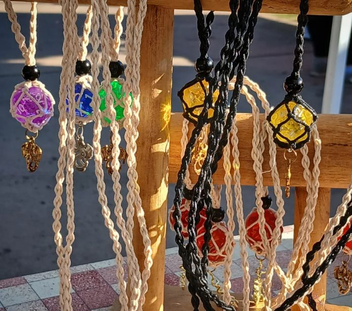 Handmade D20 necklaces hanging from a wood display at a market booth