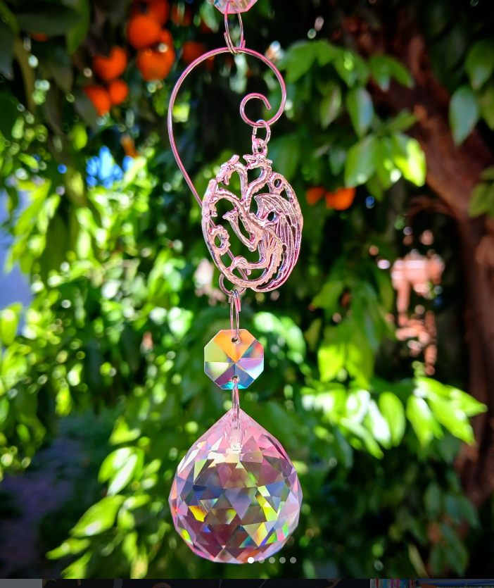 Fantasy dragon suncatcher with crystal prism hanging in bright garden light
